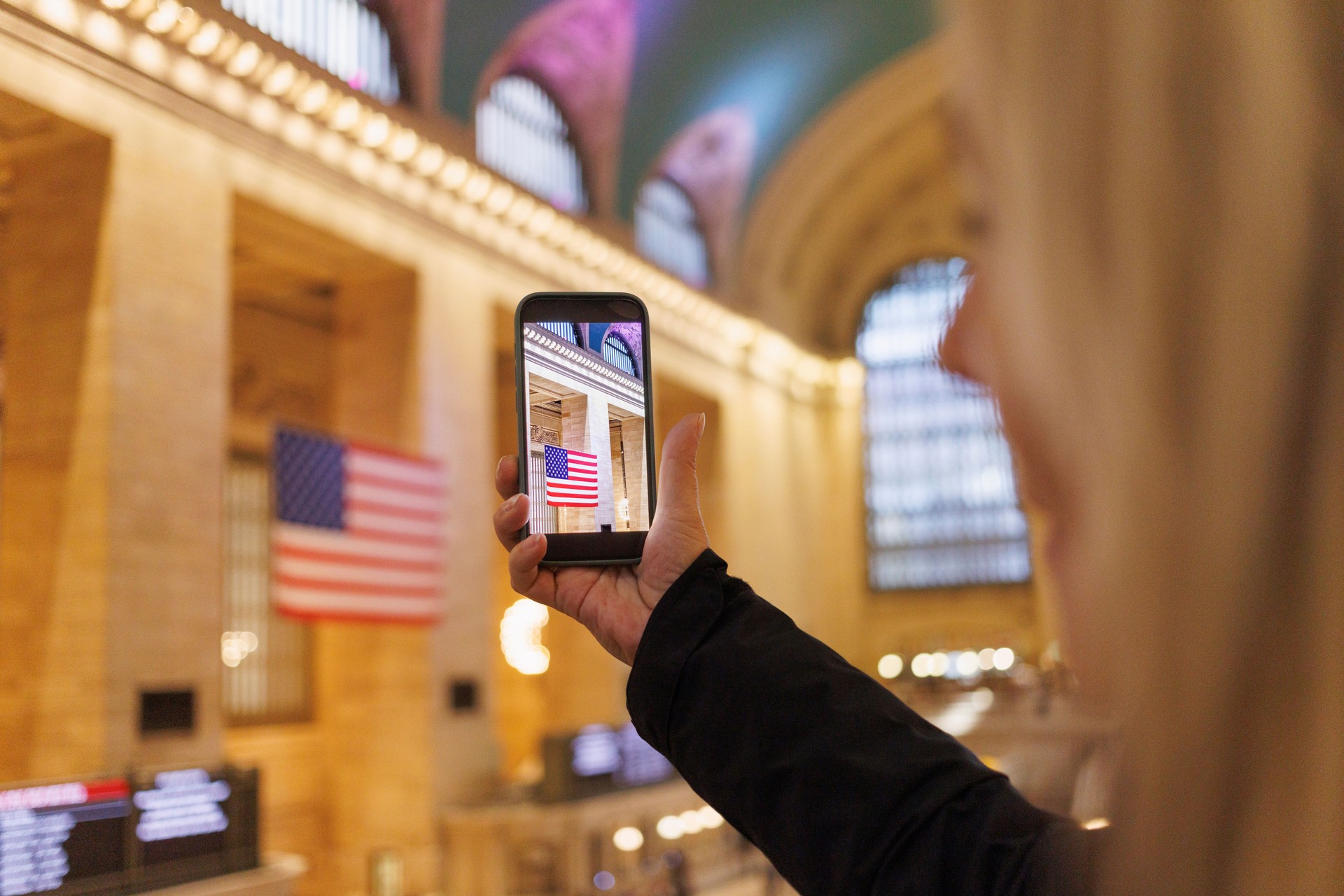 Female tourist in New York taking photos with phone. USA flag, Central Terminal station  Manhattan  NYC.